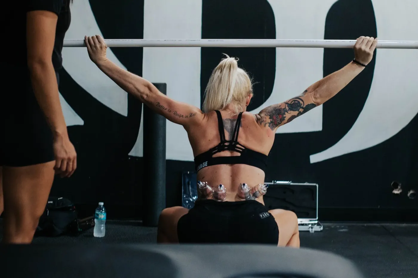 An athlete with cups on her back doing an overhead mobility exercise with a clinician beside her